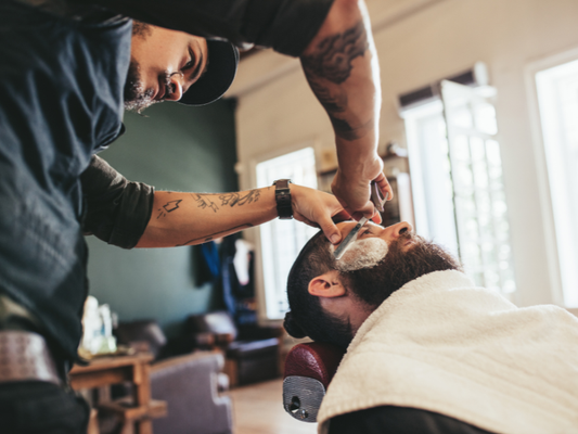 alt="barber shaving a man's beard with a straight razor in a barbershop"